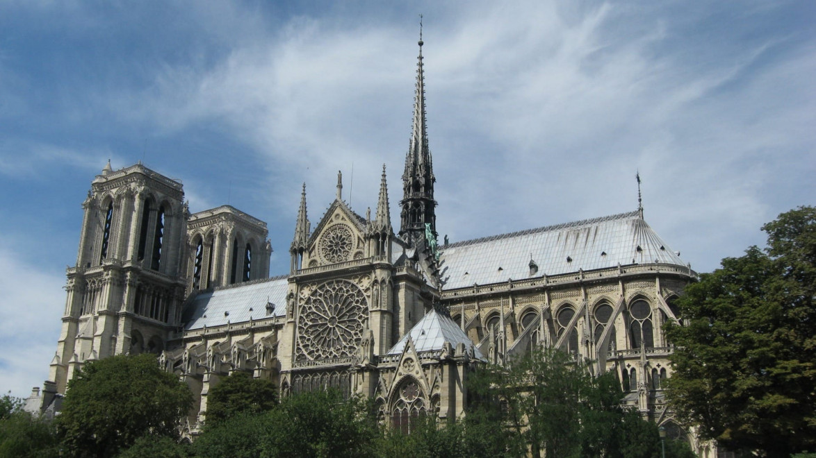 Exterior view of the historic Notre-Dame Cathedral in Paris, showcasing detailed Gothic architecture under a blue sky.