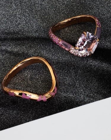 Two ornate rings with pink gemstones set on a textured surface, showcasing intricate design and elegance.