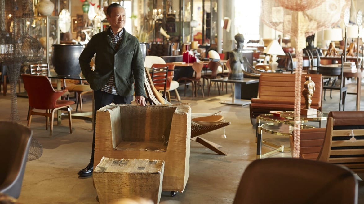 Man standing in a furniture showroom with various chairs and decorative items in the background.