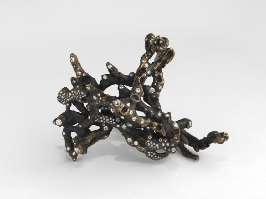 Intricate sculpture of black branches with embedded sparkling gemstones on a plain white background.