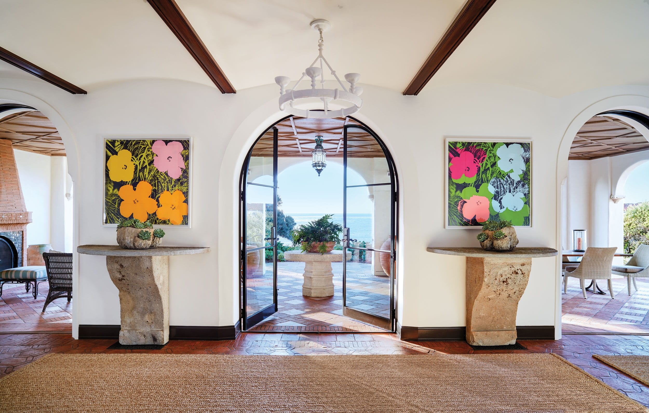 In an airy gallery with views of the Pacific, designer Madeline Stuart installed a custom-made Paul Ferrante chandelier above Andy Warhol “Flowers” paintings, 18th-century Italian stone consoles, and rugs made of woven palm matting.