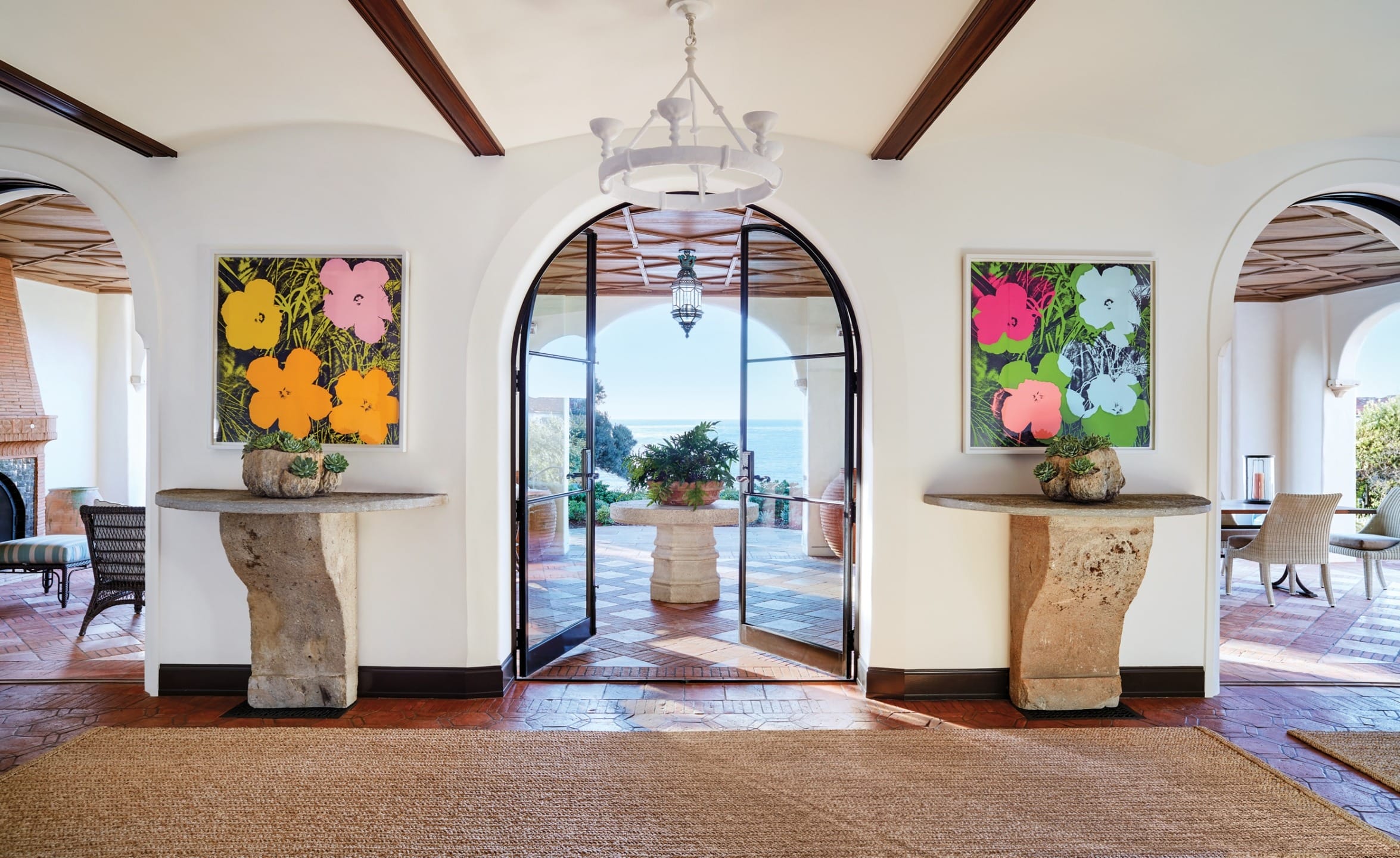Elegant Mediterranean-style foyer with ocean view, featuring colorful flower paintings and rustic stone tables.