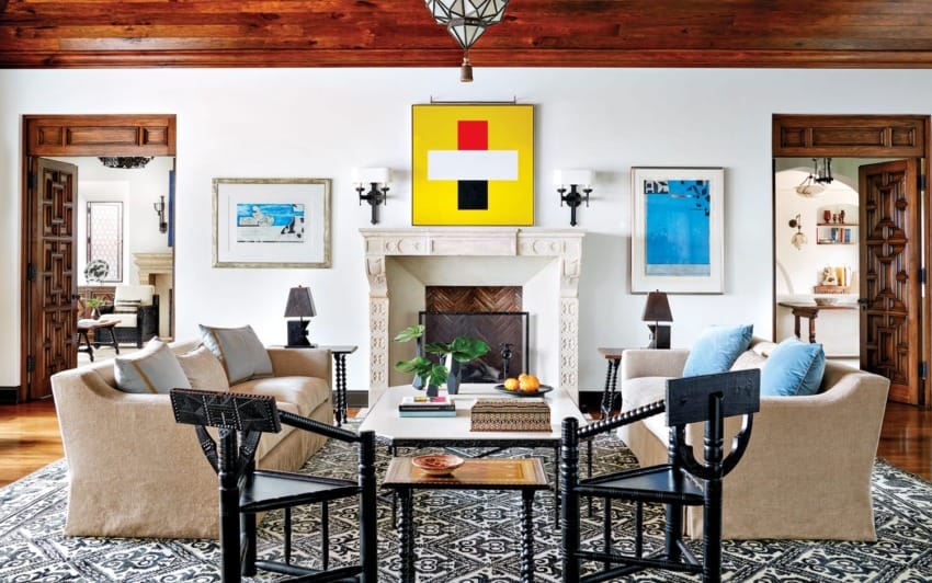 Elegant living room with beige sofas, black chairs, modern art above a fireplace, and decorative wood details.