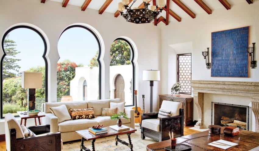 Elegant living room with arched windows, white sofas, wooden coffee table, and fireplace in a Mediterranean-style home.