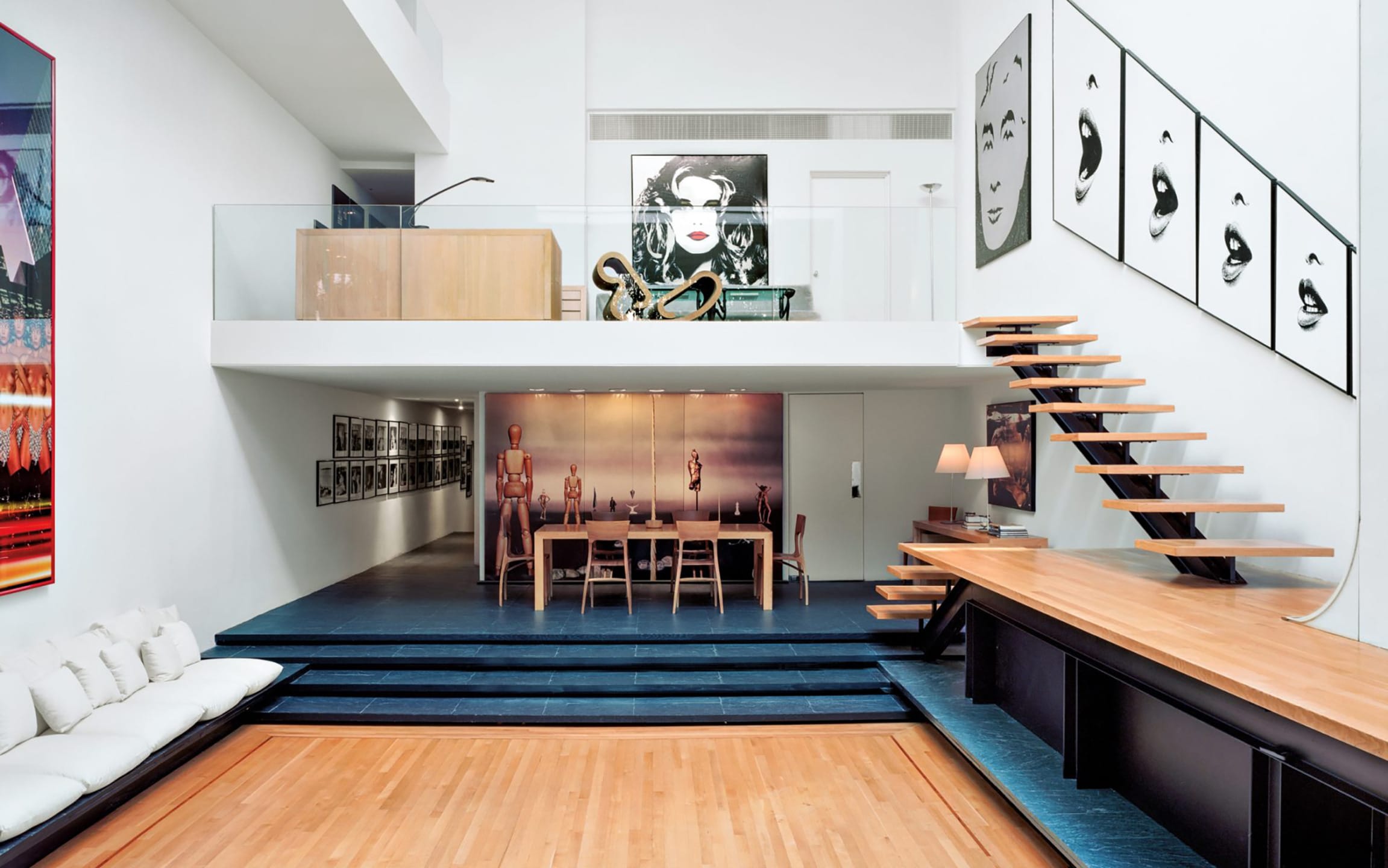 Modern loft interior with abstract art, floating staircase, dining area, and seating, showcasing contemporary design elements.