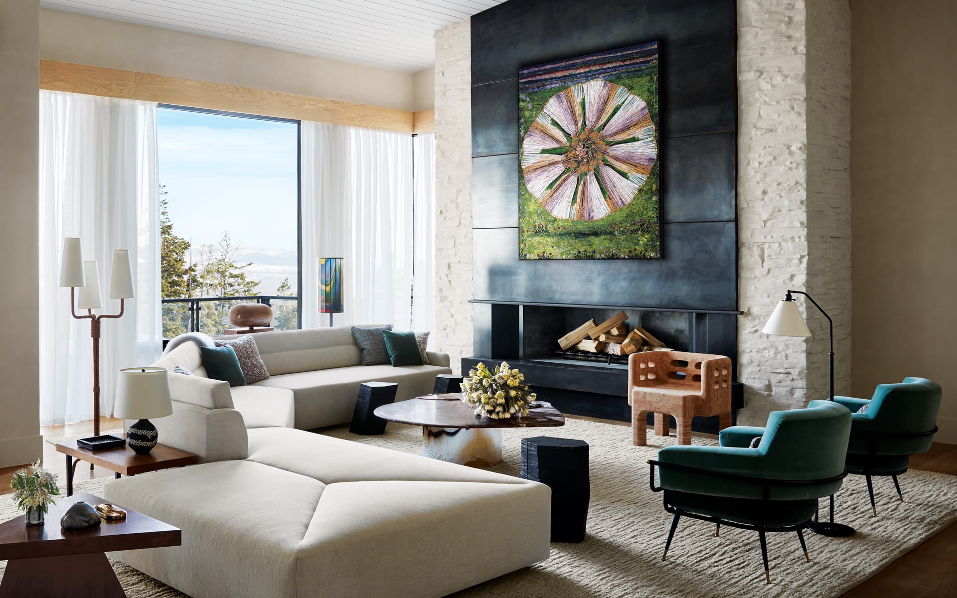Modern living room with large painting above fireplace, stylish furniture, and bright natural light from large windows.