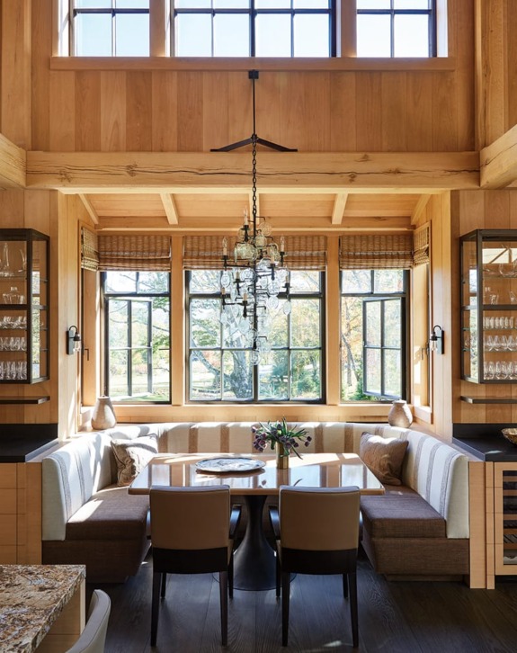 Cozy dining area with a wooden table, chairs, and chandelier, surrounded by large windows and wooden interior decor.