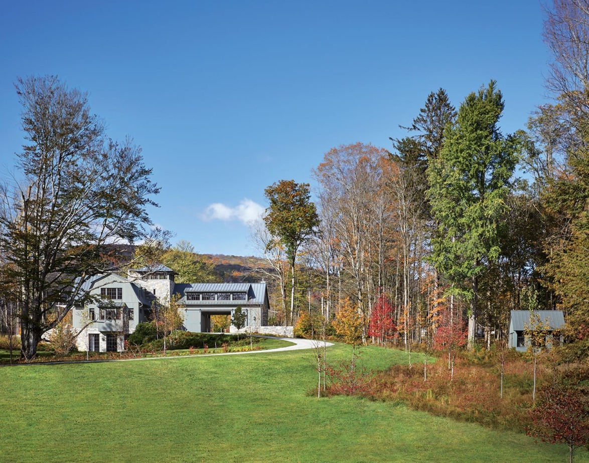 Large house surrounded by trees with a spacious lawn under a clear blue sky.
