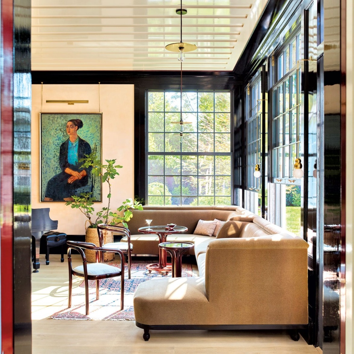 Sunny room with a large sectional sofa, a colorful portrait on the wall, and large windows overlooking a garden.