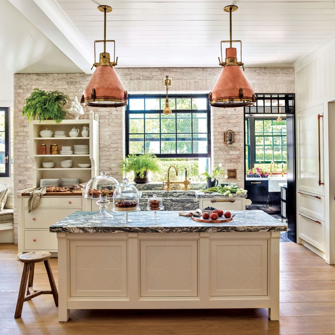 Rustic kitchen with marble island, copper pendant lights, large windows, and open shelves displaying dishes and plants.