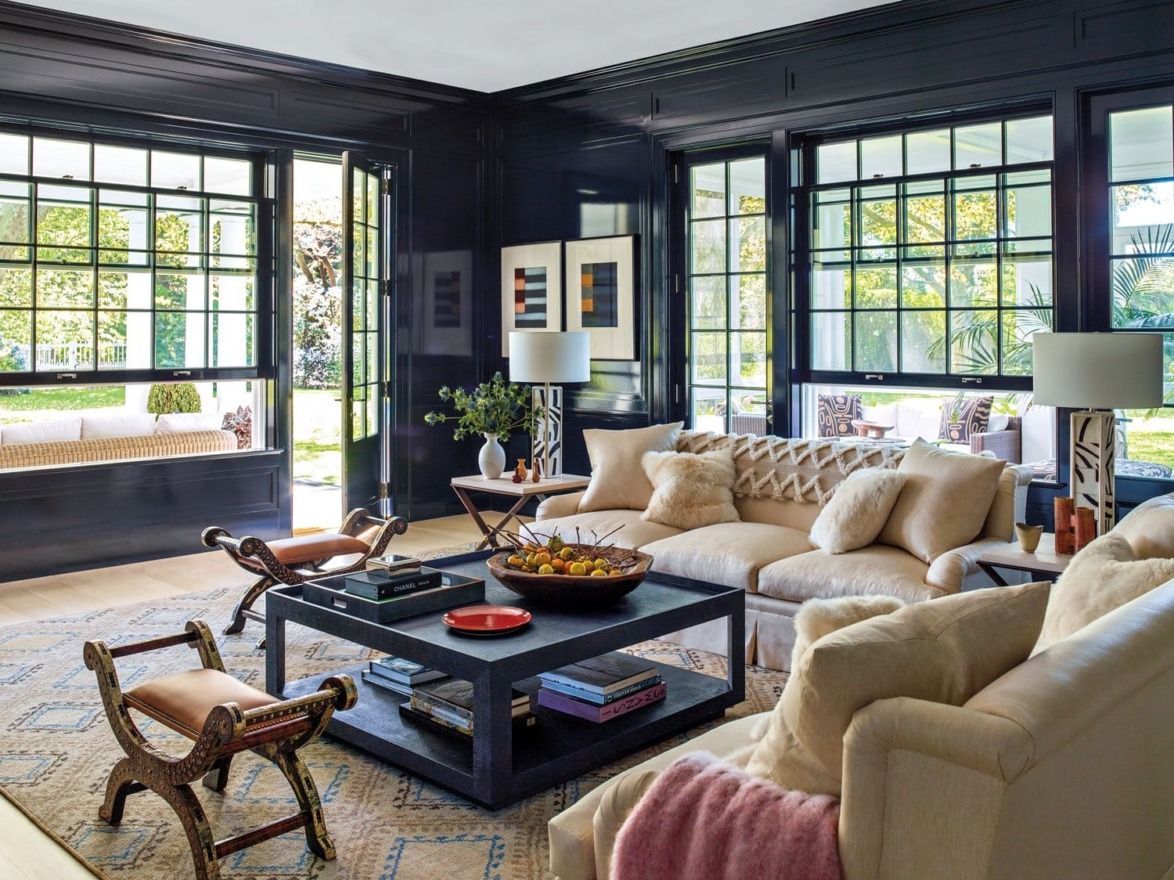 Luxurious living room with beige sofas, black walls, large windows, and a central coffee table adorned with fruit bowl.