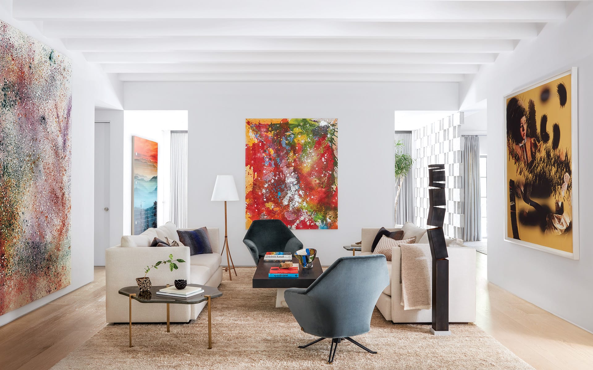 Modern living room with abstract art, colorful paintings, white walls, and contemporary furniture, including sofas and armchairs.