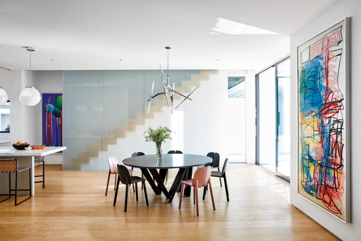 Modern dining room with round table, mixed chairs, abstract art, and large windows.