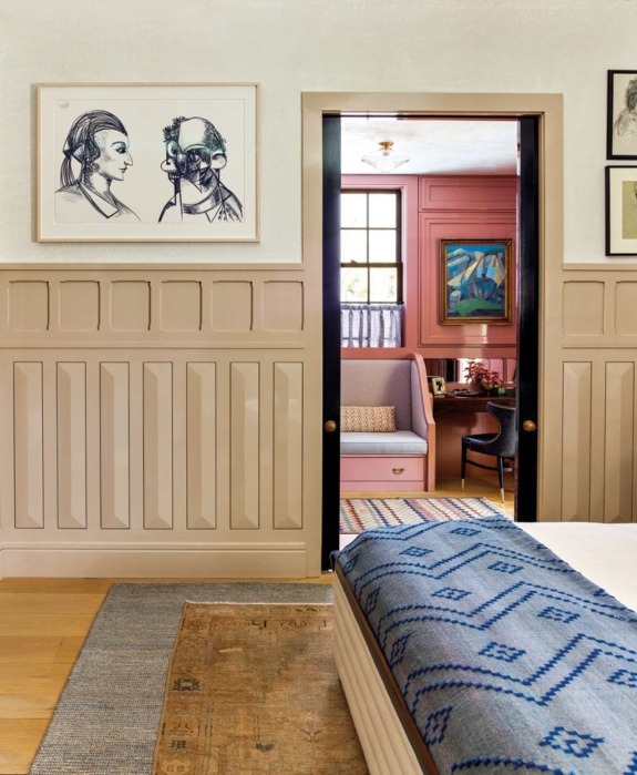 Artistic bedroom view with framed sketches on a paneled wall and an open door leading to a colorful adjoining room.