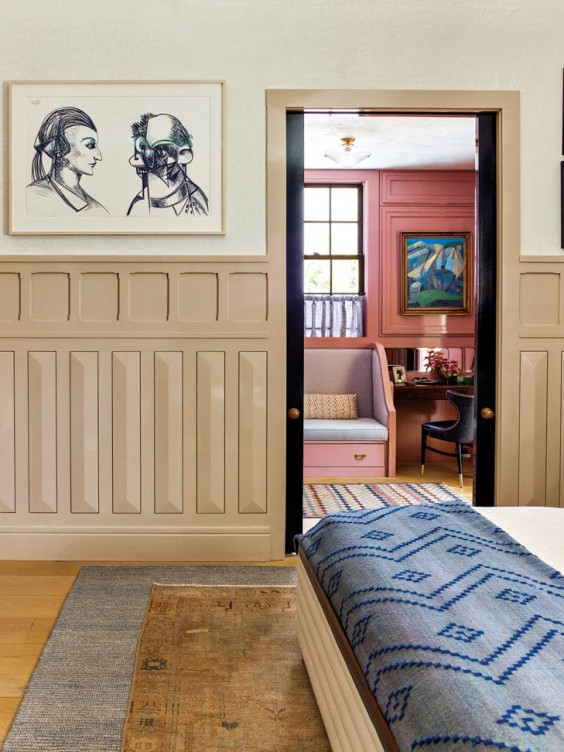 Artistic bedroom view with framed sketches on a paneled wall and an open door leading to a colorful adjoining room.