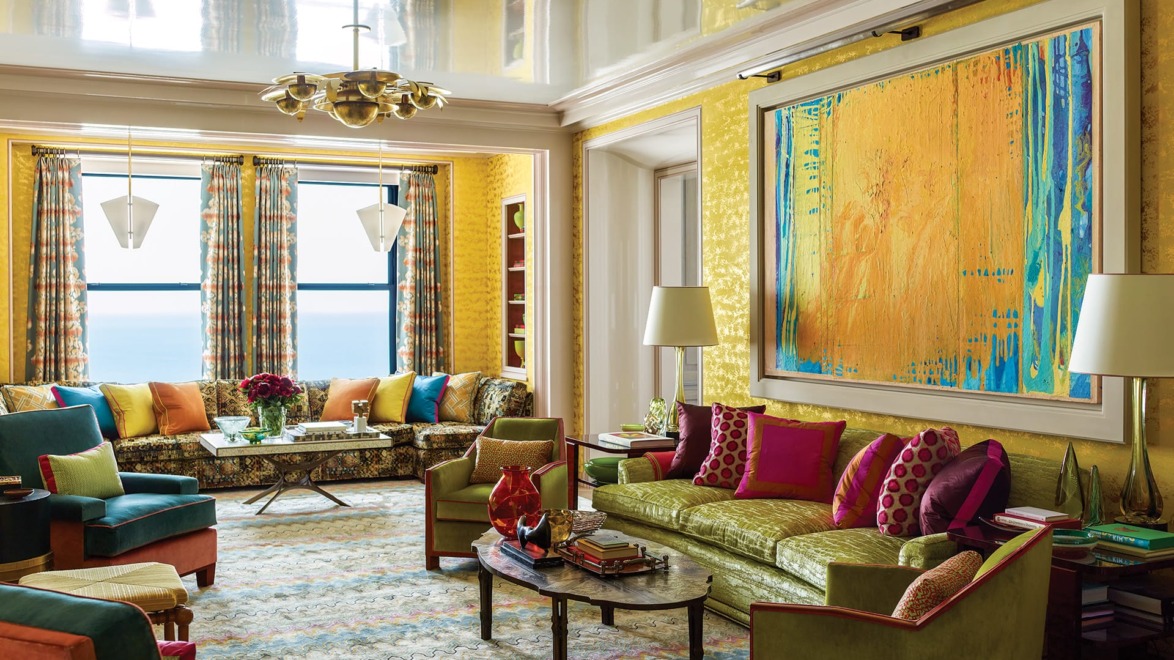 Colorful living room with vibrant sofas, patterned rugs, large abstract painting, and ceiling lights.
