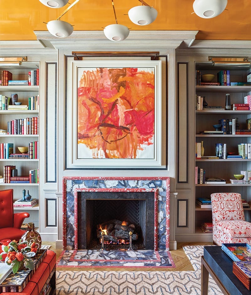 Colorful living room with abstract painting above a fireplace, surrounded by bookshelves filled with books and decor items.
