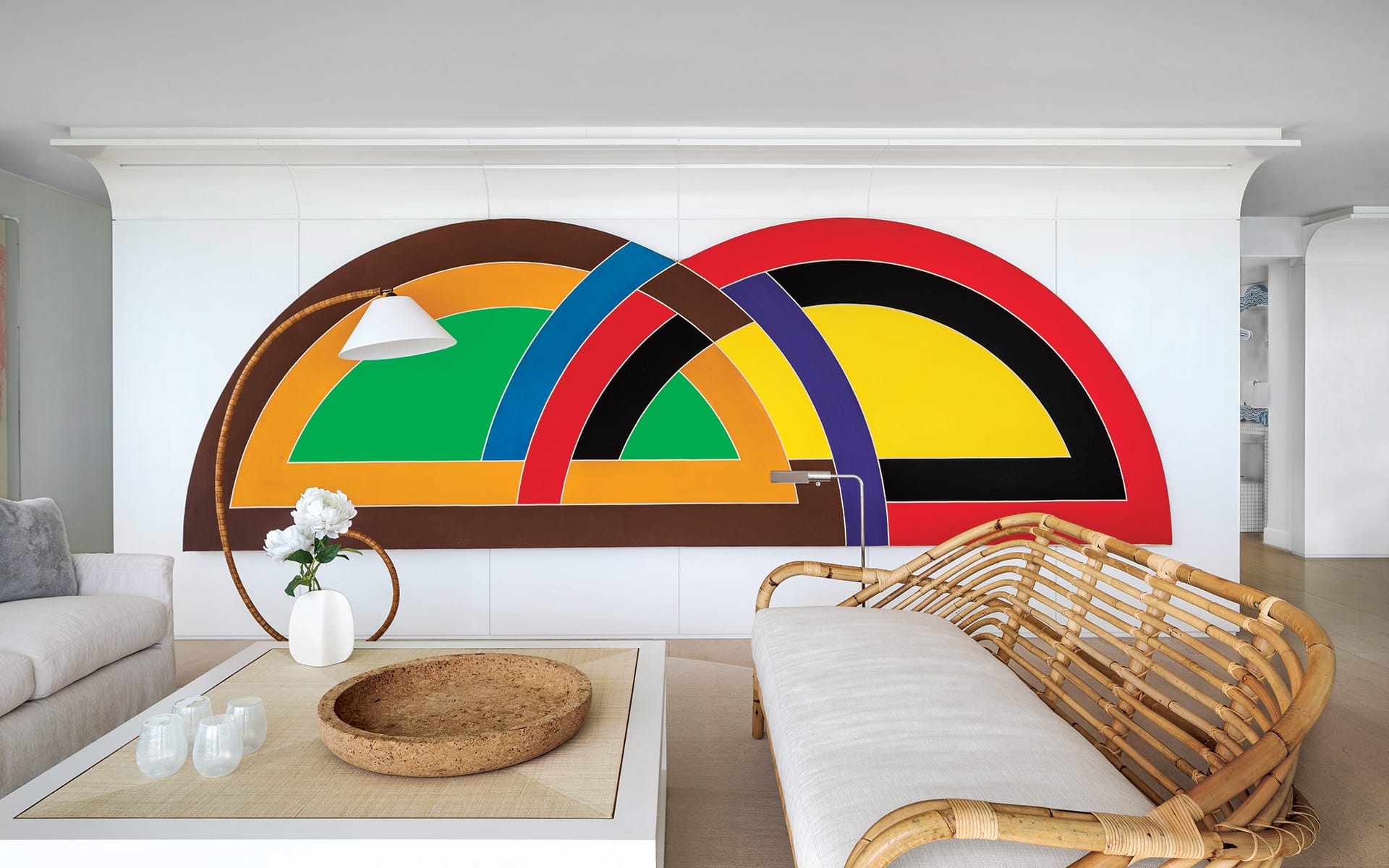 Colorful abstract wall art above a modern sofa in a stylish living room with a rattan chair and a floral centerpiece.