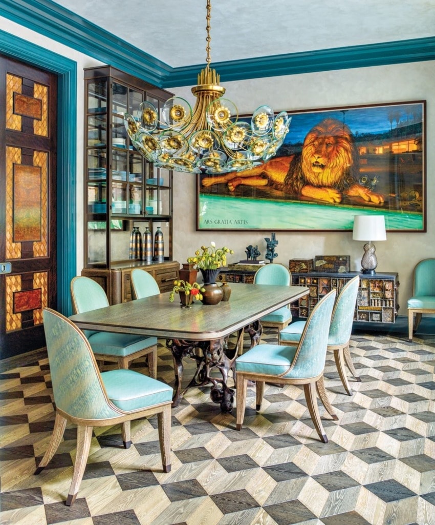Elegant dining room with ornate chandelier, large lion painting, patterned floor, and wooden table surrounded by teal chairs.