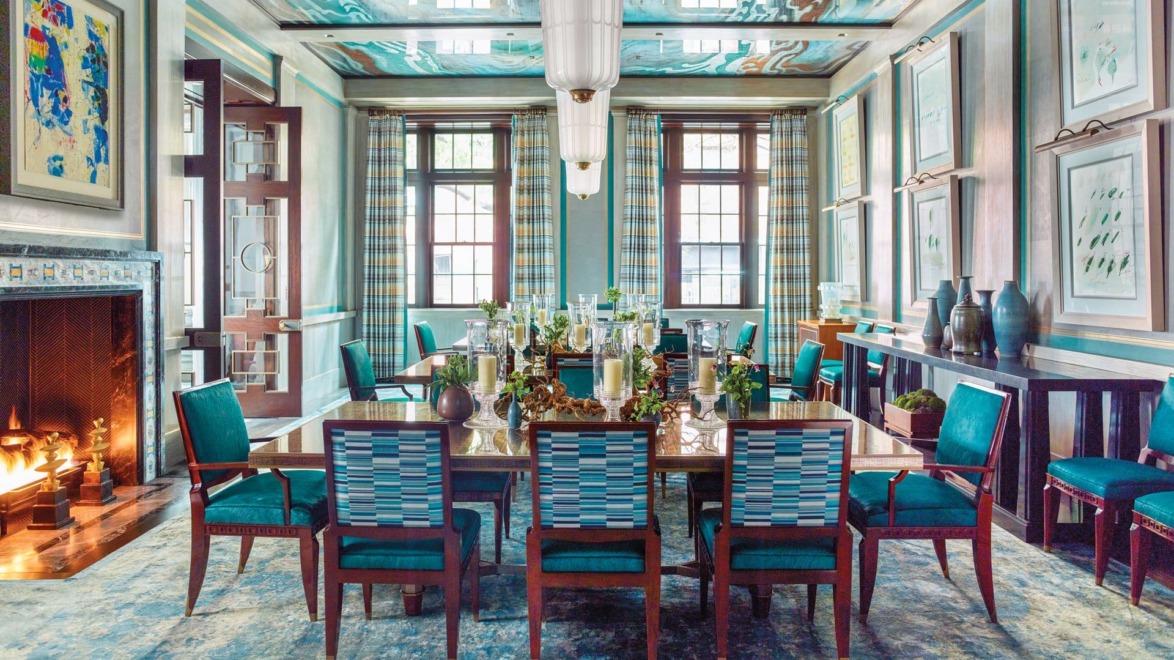 Elegant dining room with a long table, teal chairs, artwork, and a cozy fireplace, decorated in a modern style.