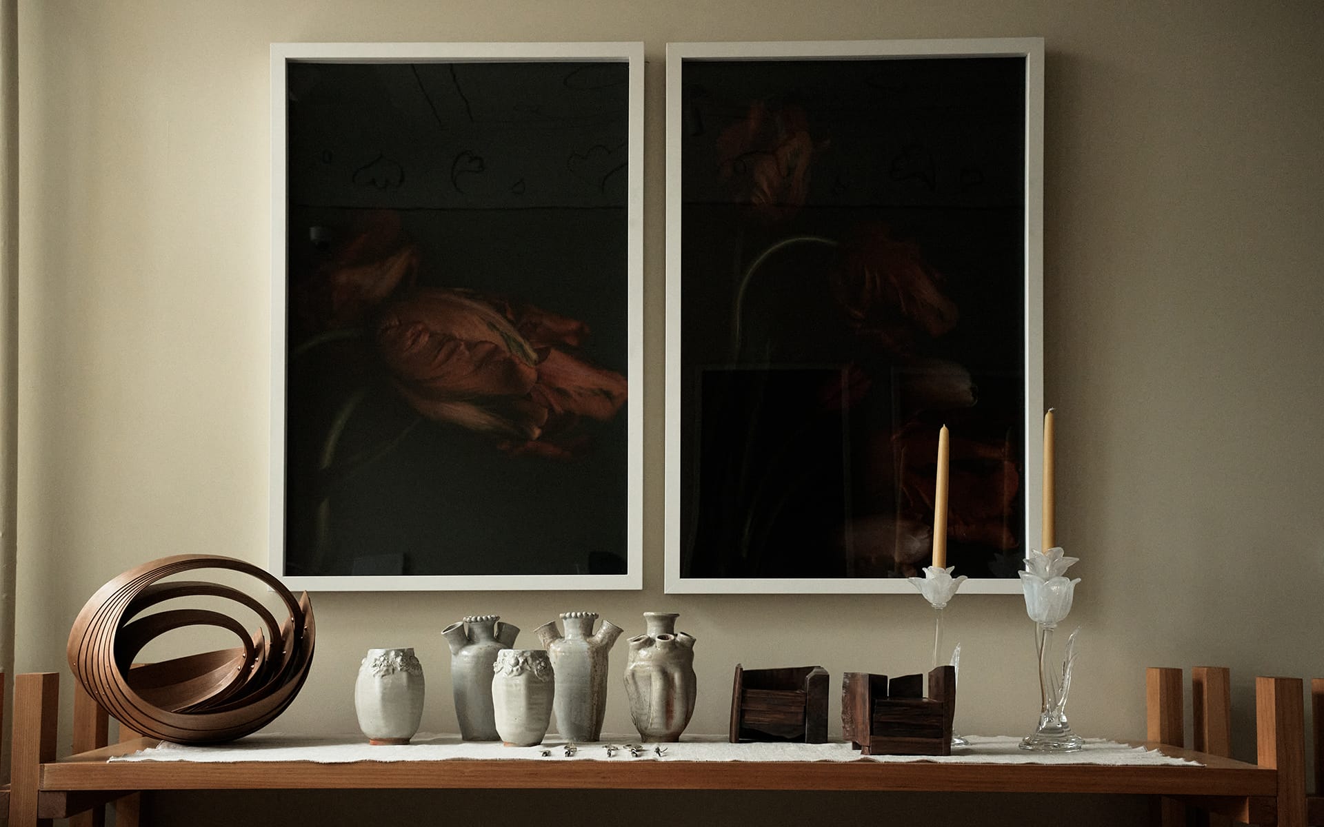 Elegant table with pottery, candles, and decor, set against a backdrop of two framed artworks featuring flowers.