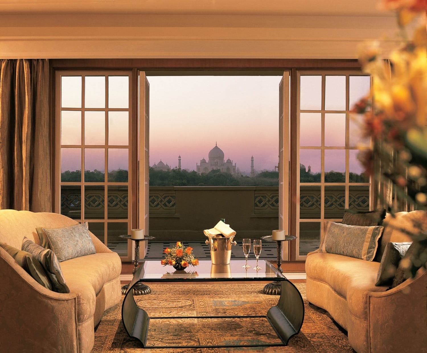 View of the Taj Mahal from a luxurious hotel room with a cozy seating area, champagne, and a decorative flower arrangement on the table.