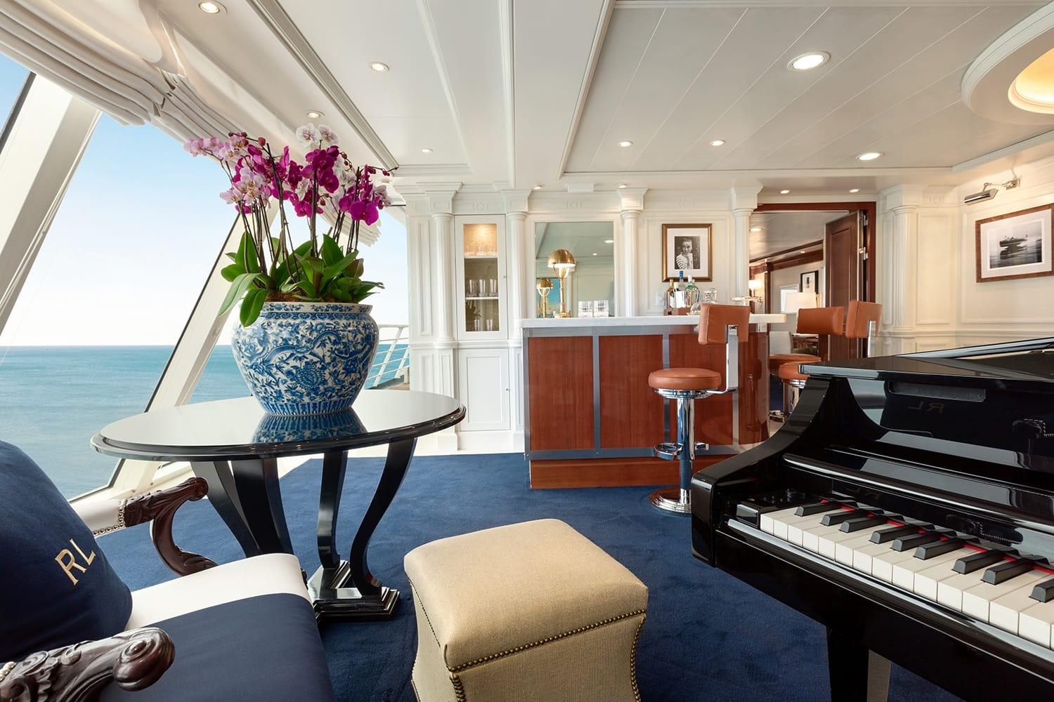 Luxurious ship lounge with grand piano, potted orchids on a table, ocean view, and wooden bar with stools.