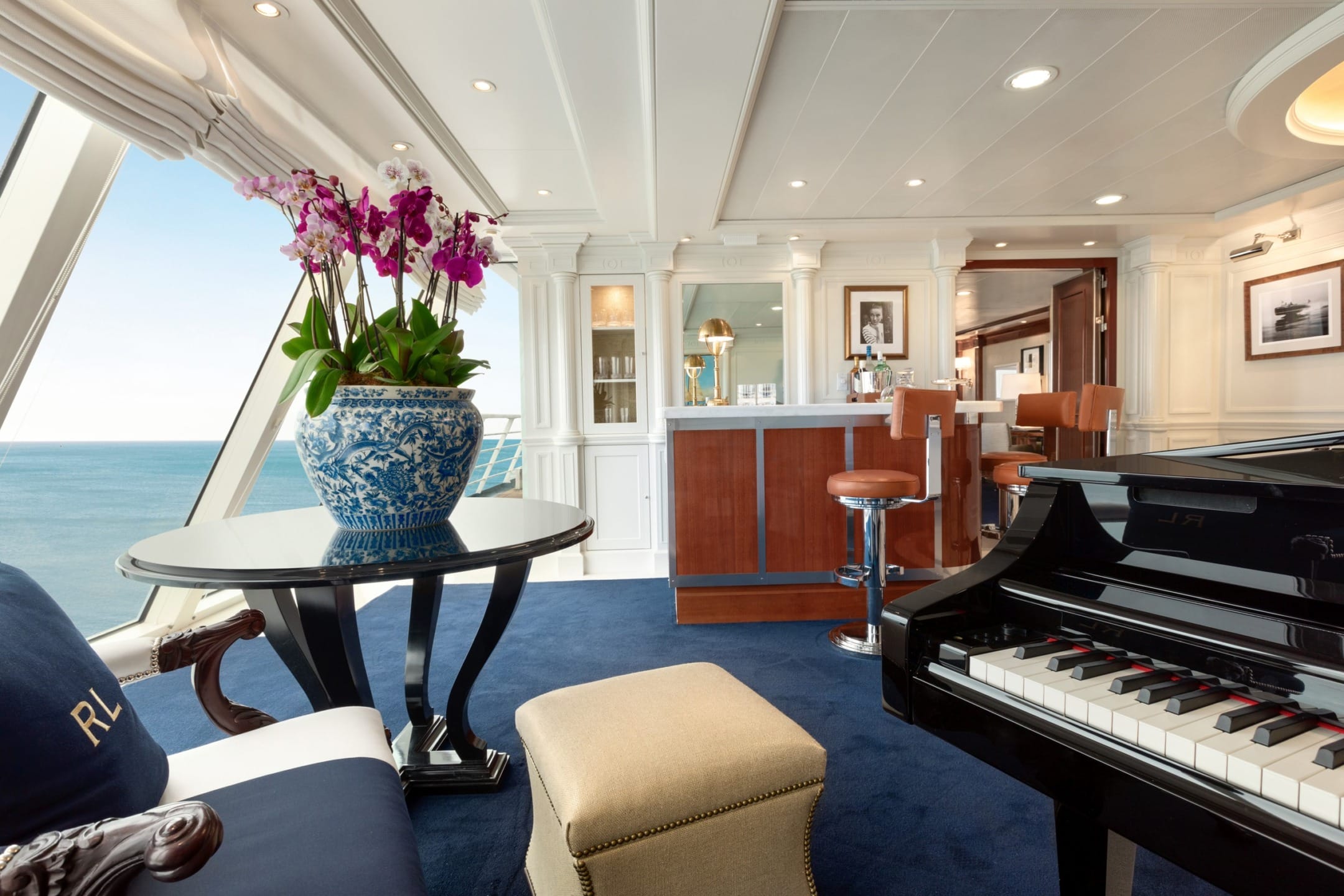 Luxurious yacht interior with grand piano, elegant bar, blue carpet, and ocean view.