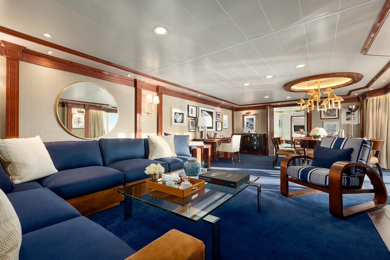 Luxurious yacht interior with blue and white decor, large circular mirror, elegant furniture, and modern lighting fixtures.
