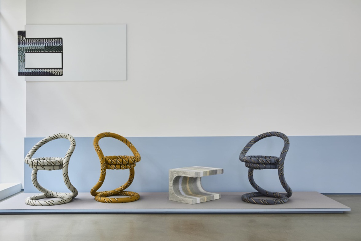 Three uniquely shaped chairs with zigzag patterns and a small, modern table in a minimalist room with a blue and white wall.