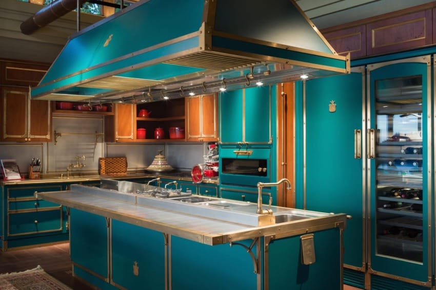 Luxury teal kitchen with stainless steel appliances, central island, and wooden cabinets, illuminated by modern lighting.