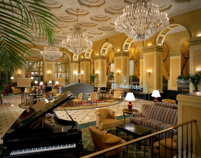 Elegant hotel lobby with grand piano, chandeliers, plush seating, and ornate details, creating a luxurious atmosphere.