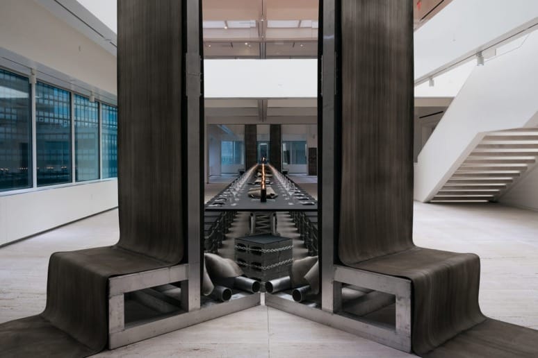 Modern art installation with reflective surfaces in a spacious gallery setting, featuring industrial metal elements.