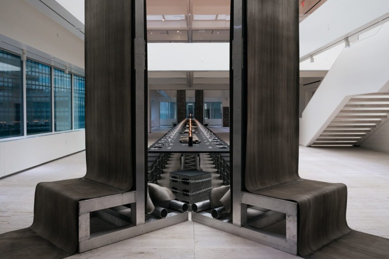 Modern art installation with reflective surfaces in a spacious gallery setting, featuring industrial metal elements.