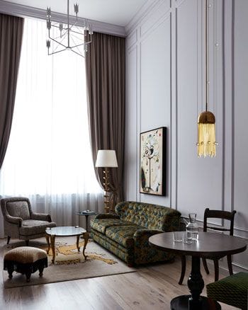 Elegant living room with high ceilings, dark drapes, vintage furniture, artwork on wall, and pendant lamp.