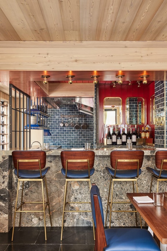 Trendy restaurant interior with a stone bar, blue barstools, and modern light fixtures in a cozy, stylish setting.