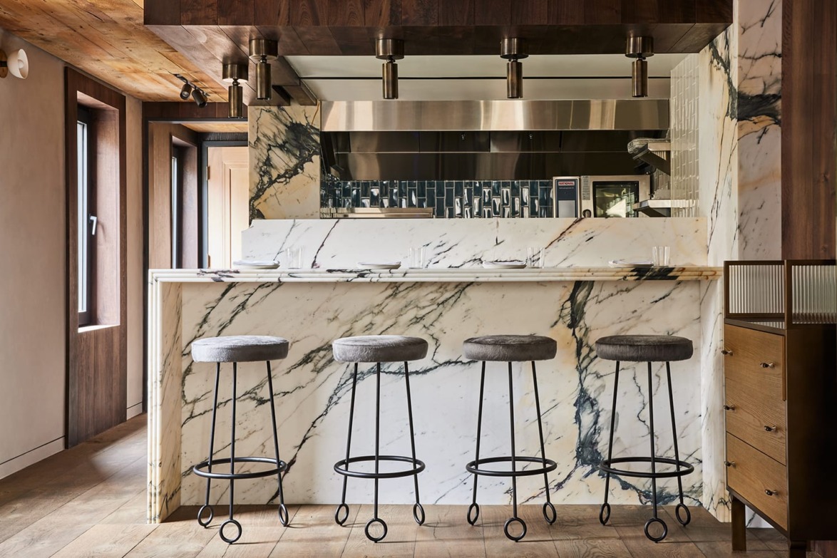 Modern kitchen with marble island, high stools, and a sleek backsplash design, featuring warm wooden and metal accents.