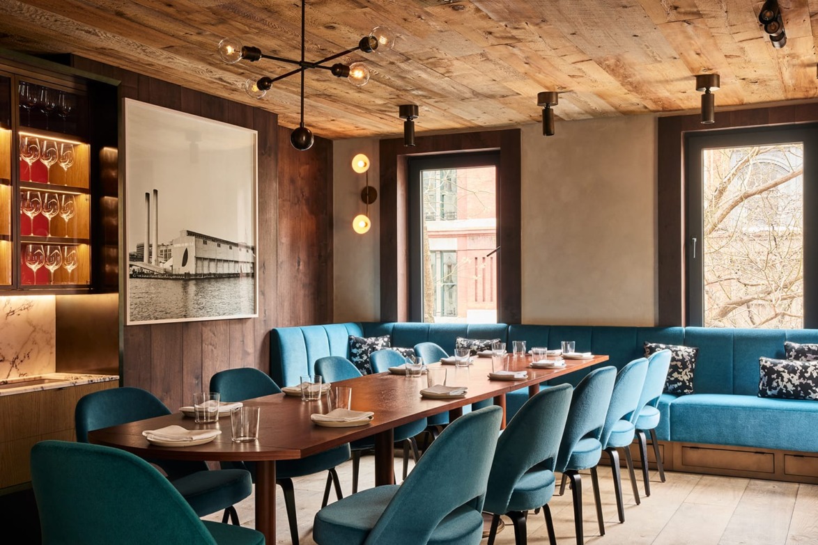 Elegant restaurant interior with a long dining table, blue chairs, and artwork on the wall.