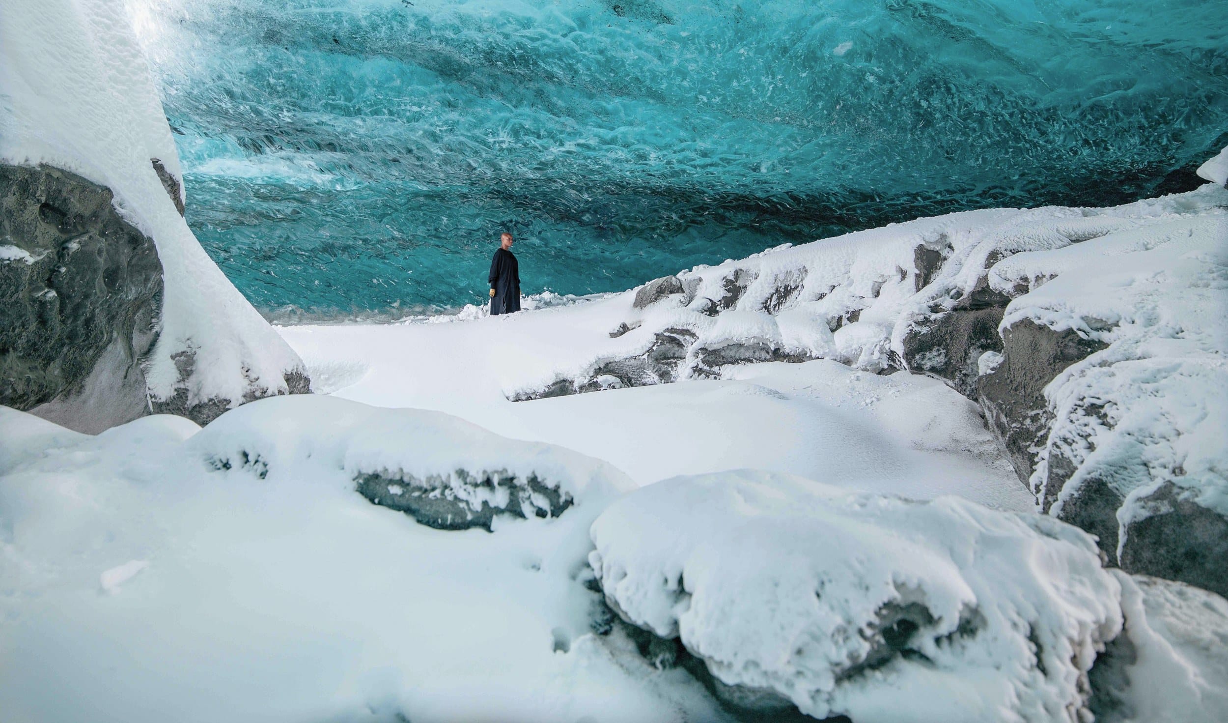 Person standing in a snow-covered ice cave with a vibrant blue ceiling.