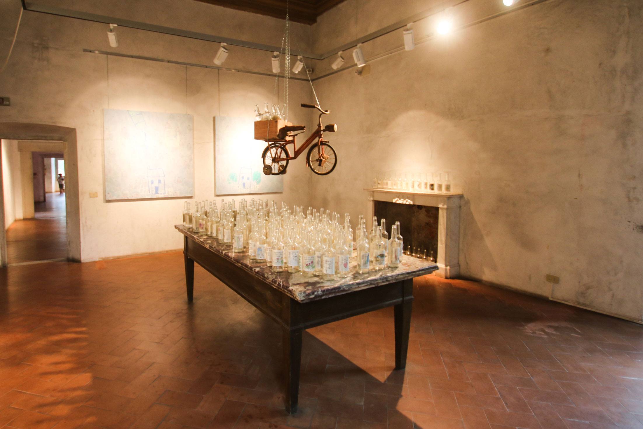 Art installation with bicycle and bottles in a minimalist gallery setting with warm lighting.