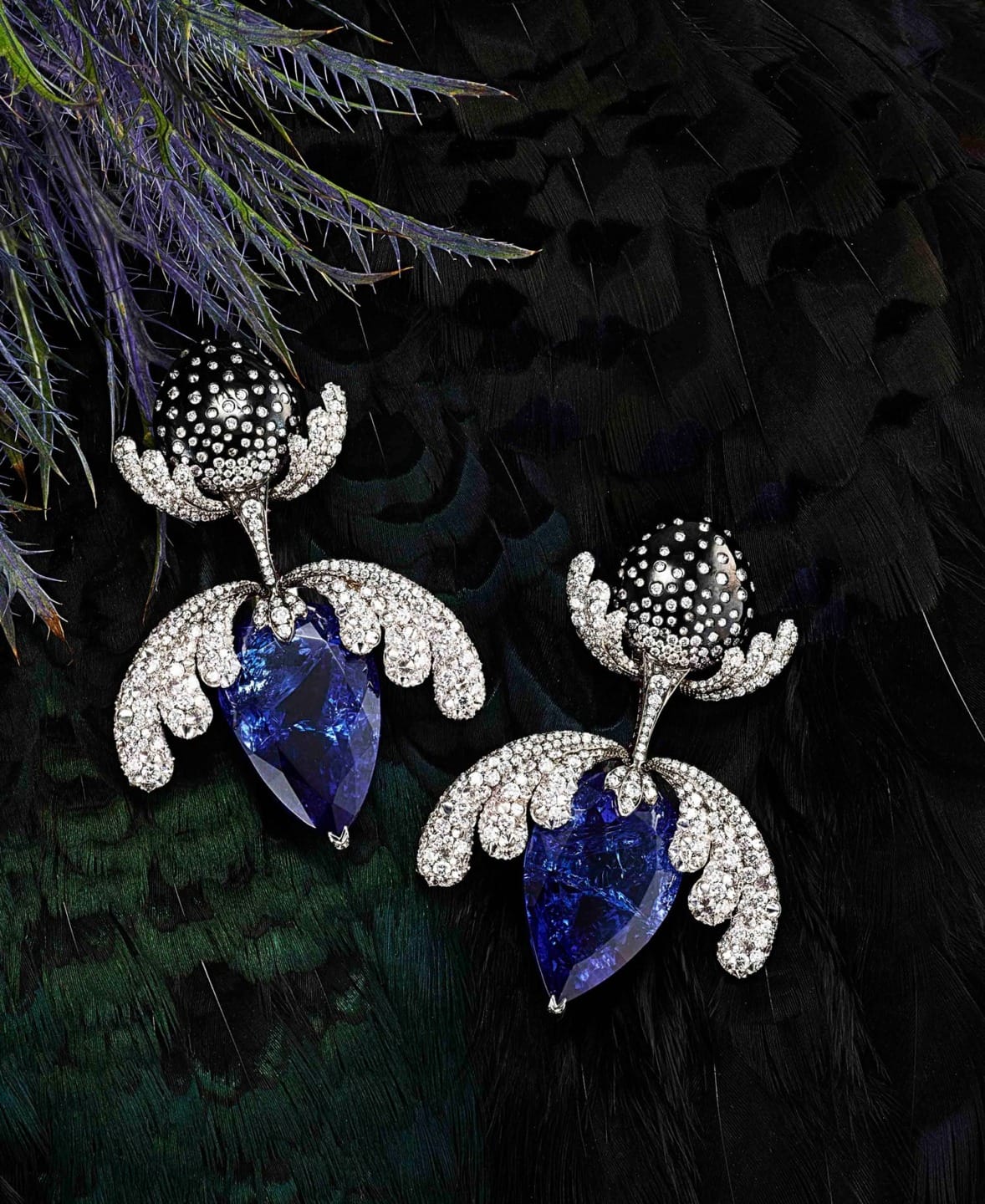 Intricate earrings with large blue gemstones and silver details on a dark feathered background.