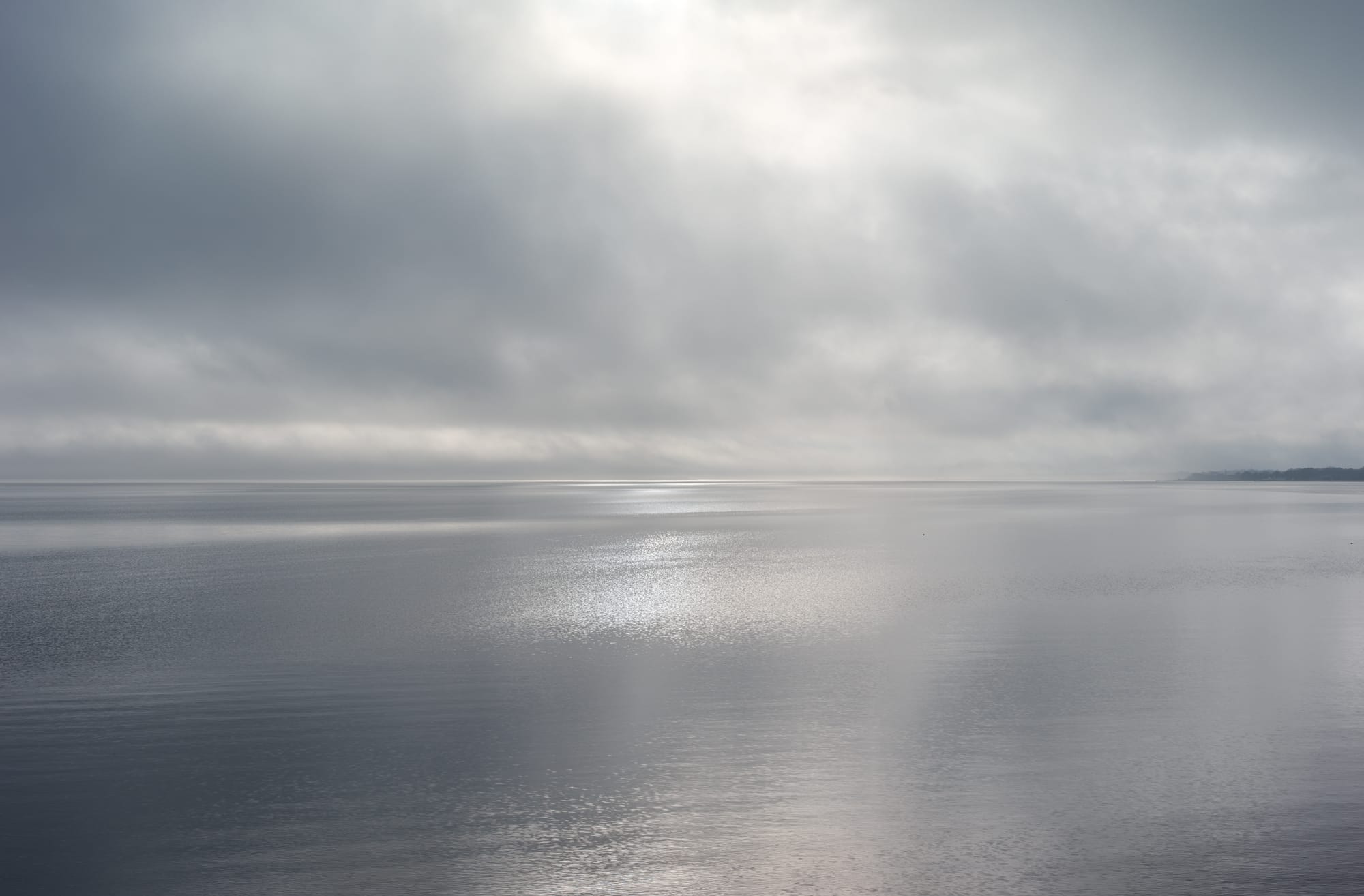 Calm sea under a cloudy, overcast sky with subtle light reflections on the water's surface.