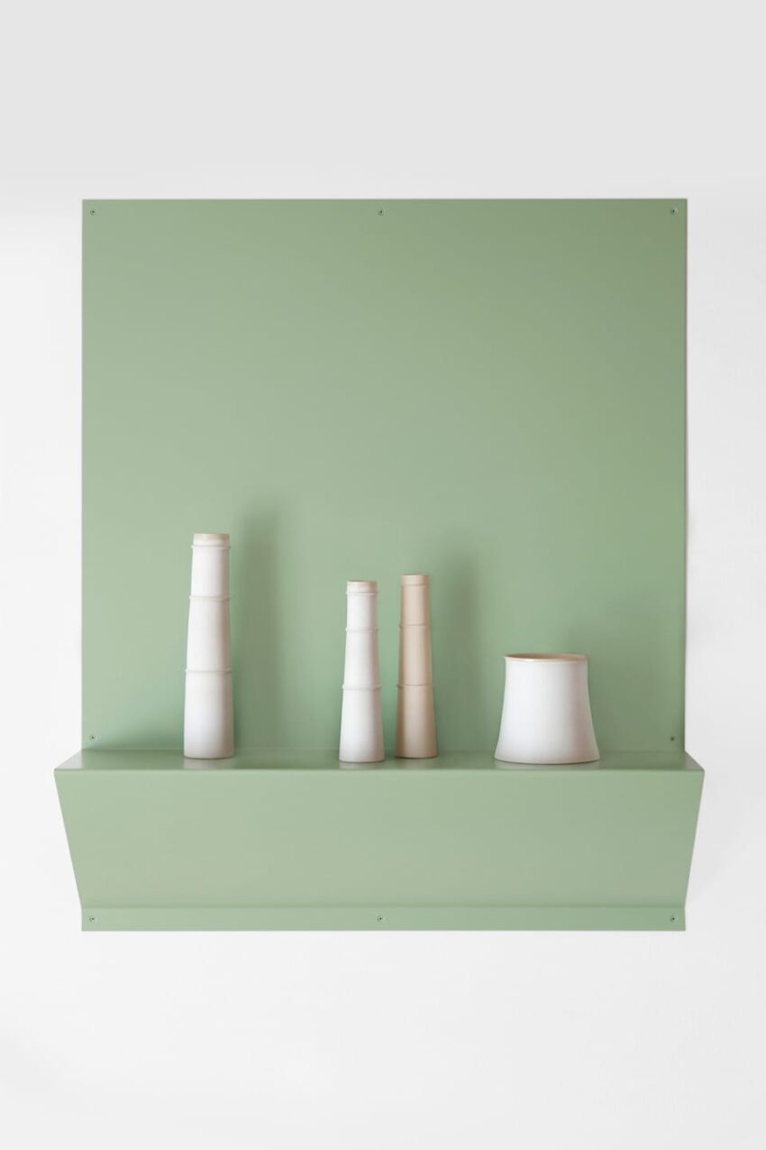 Green shelf with four white ceramic vases of varying heights and shapes placed against a pale green wall background.