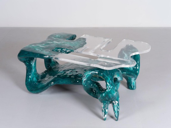Artistic coffee table with a unique, abstract turquoise base and a transparent, irregularly shaped glass top.