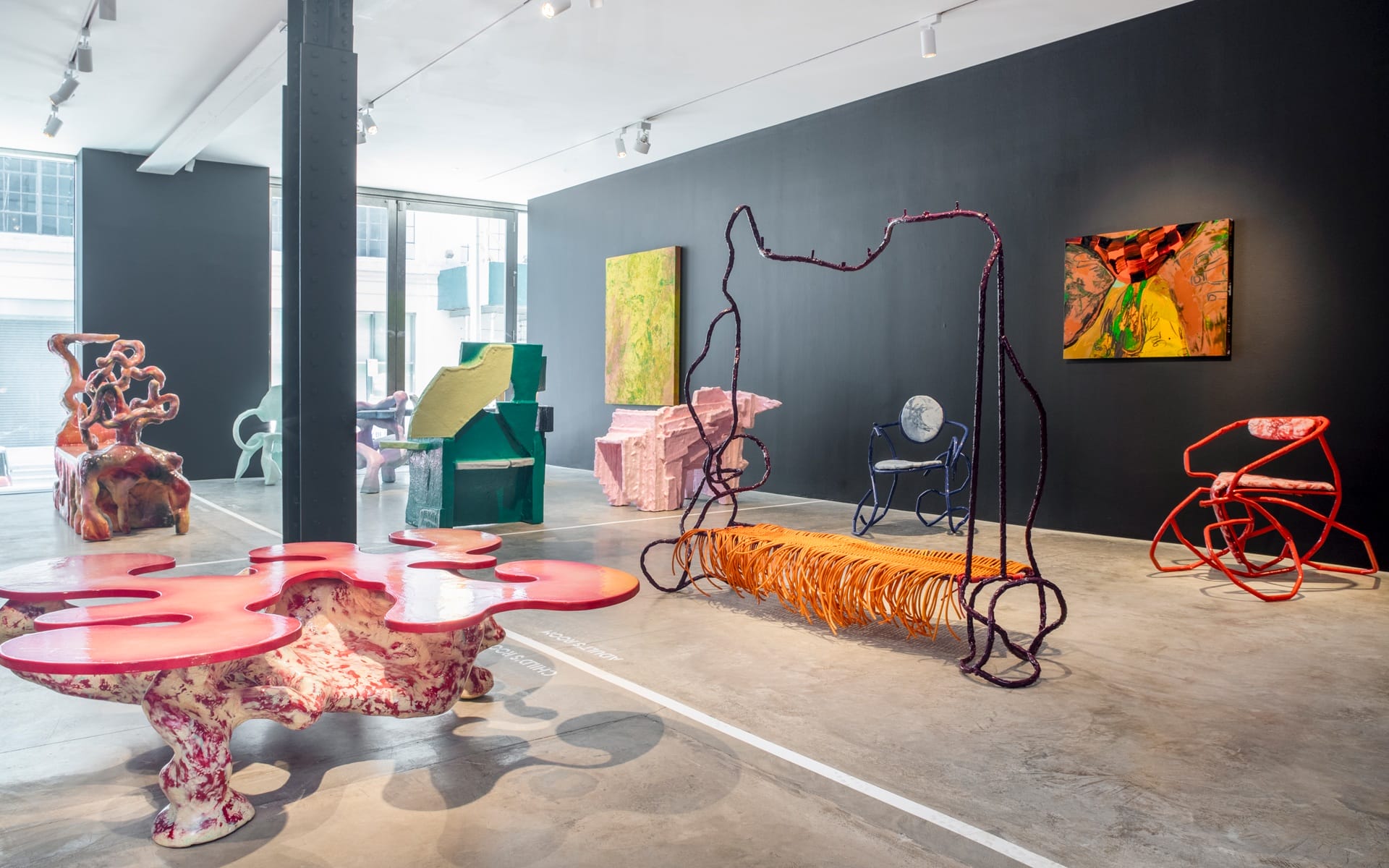 Contemporary art gallery interior with colorful modern sculptures and abstract paintings displayed on dark walls.