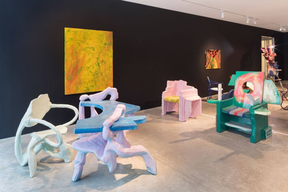 Colorful abstract furniture and paintings in a modern art gallery with a black wall and concrete floor.