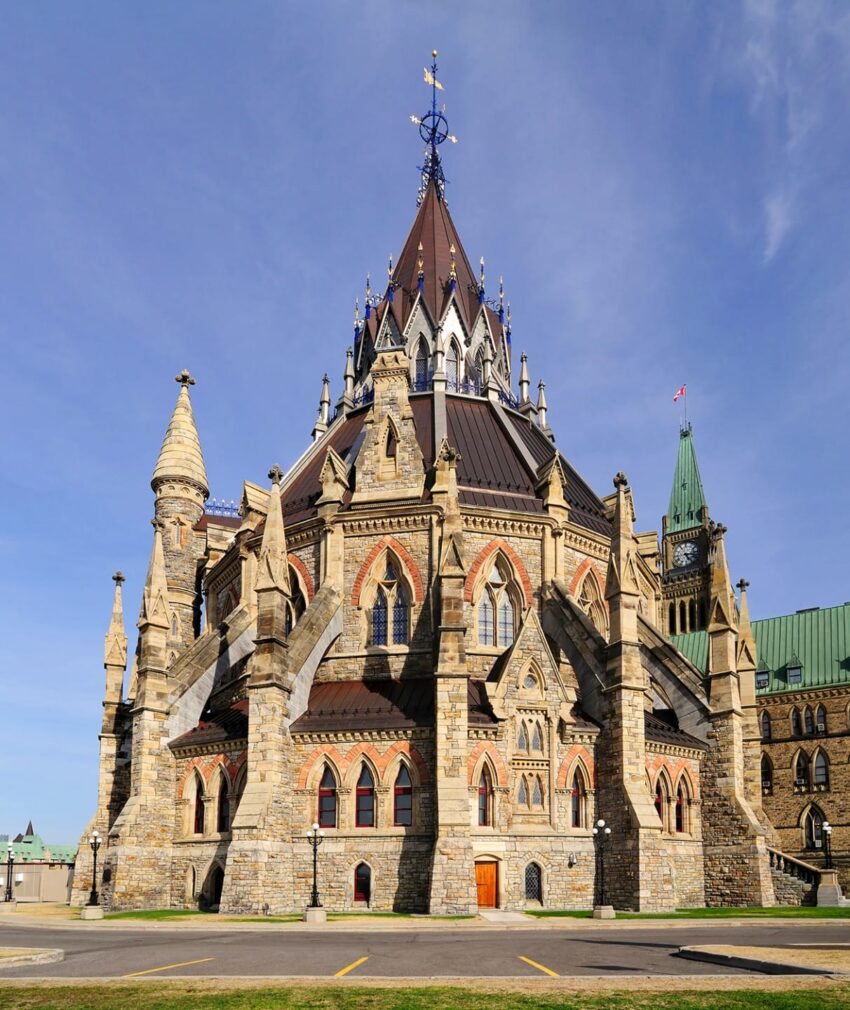 Library of Parliament in Ottawa with Gothic Revival architecture, featuring spires and buttresses, under a clear blue sky.