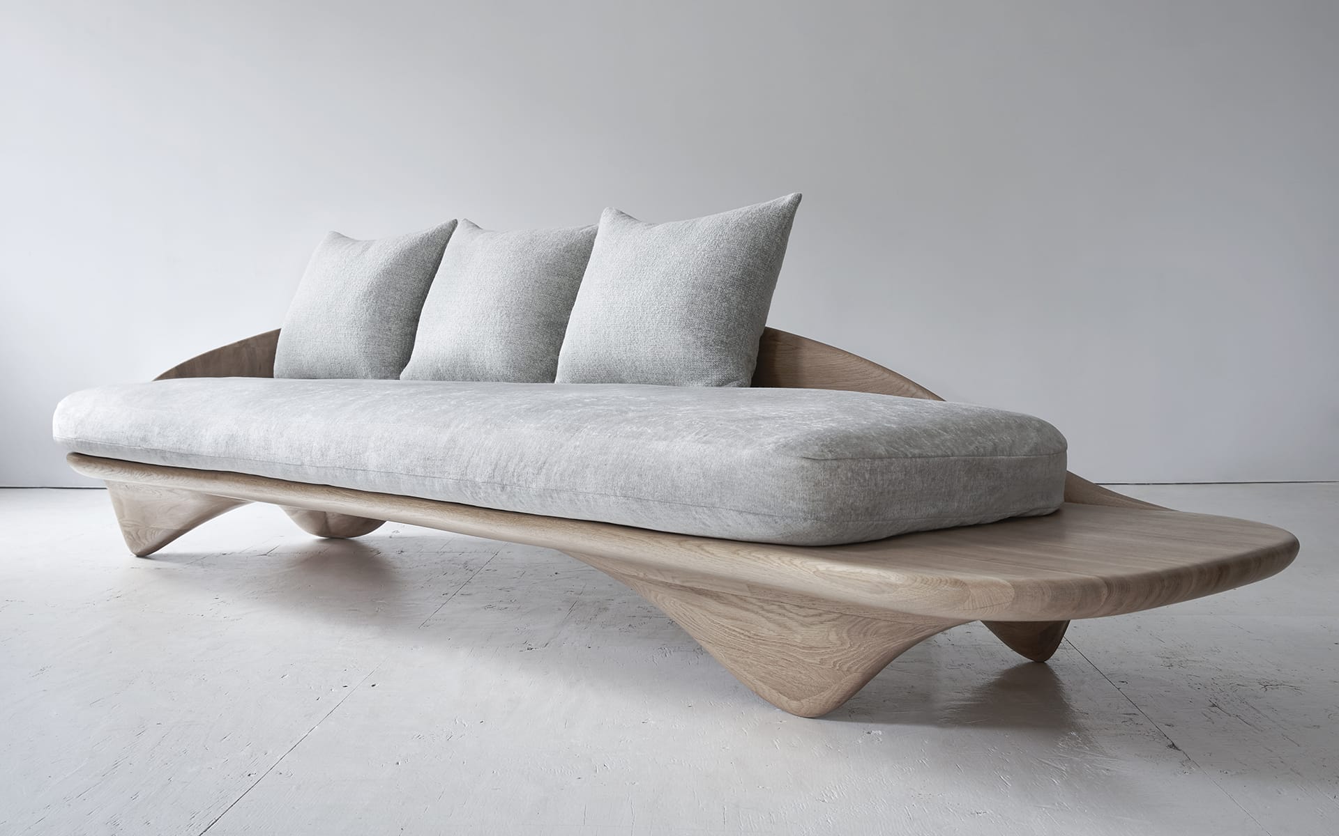 Modern wooden sofa with gray cushions on a white floor and background.
