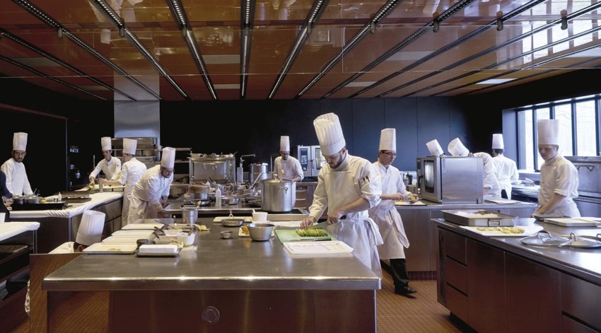 Chefs in white uniforms and hats busy preparing food in a large modern kitchen setting.