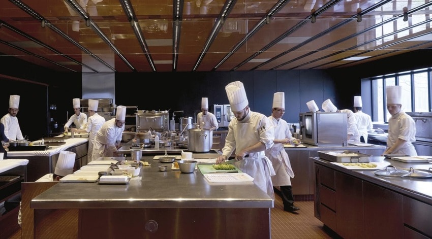 Chefs in white uniforms and hats busy preparing food in a large modern kitchen setting.